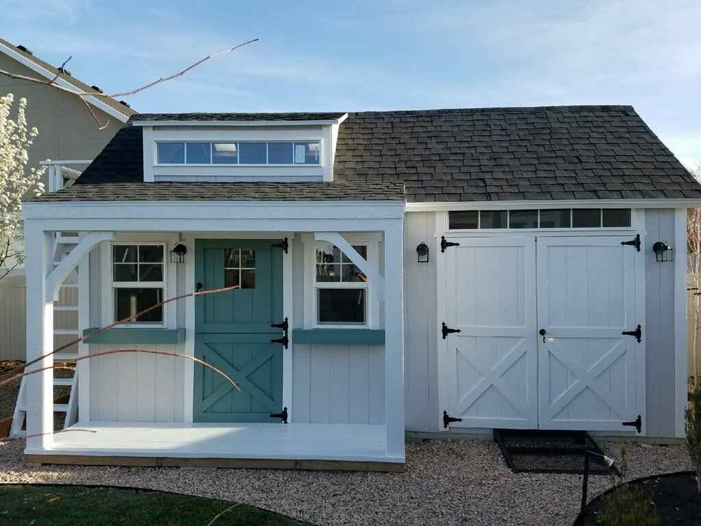 A charming shed with a playhouse section, featuring a teal door and double garage doors.