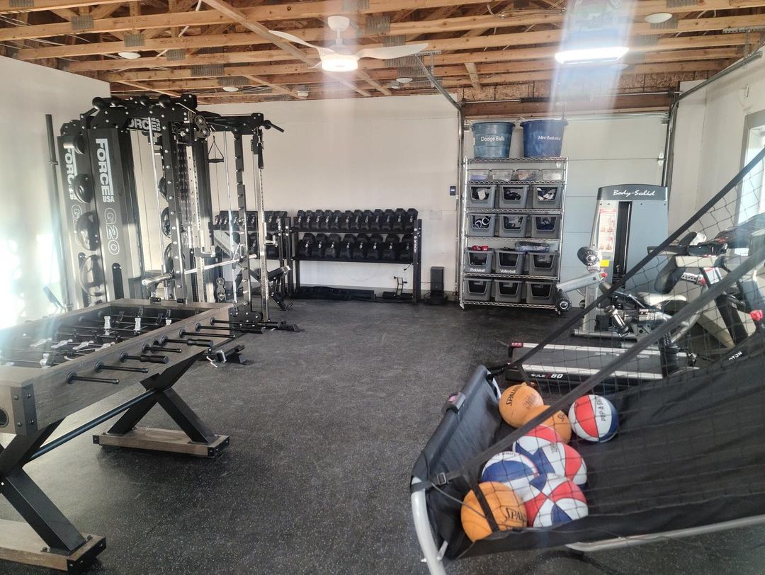 A fully-equipped home gym inside a pole barn shed, featuring weights, machines, and sports equipment.