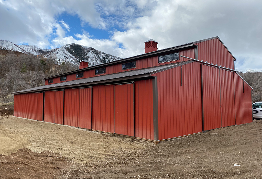 Image of a custom red pole barn with multiple storage doors and mountain backdrop.