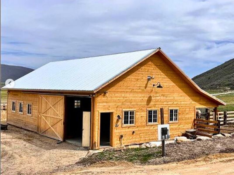 Image of a wooden pole barn with a white roof, large doors, and windows. Ideal for farming or storage.