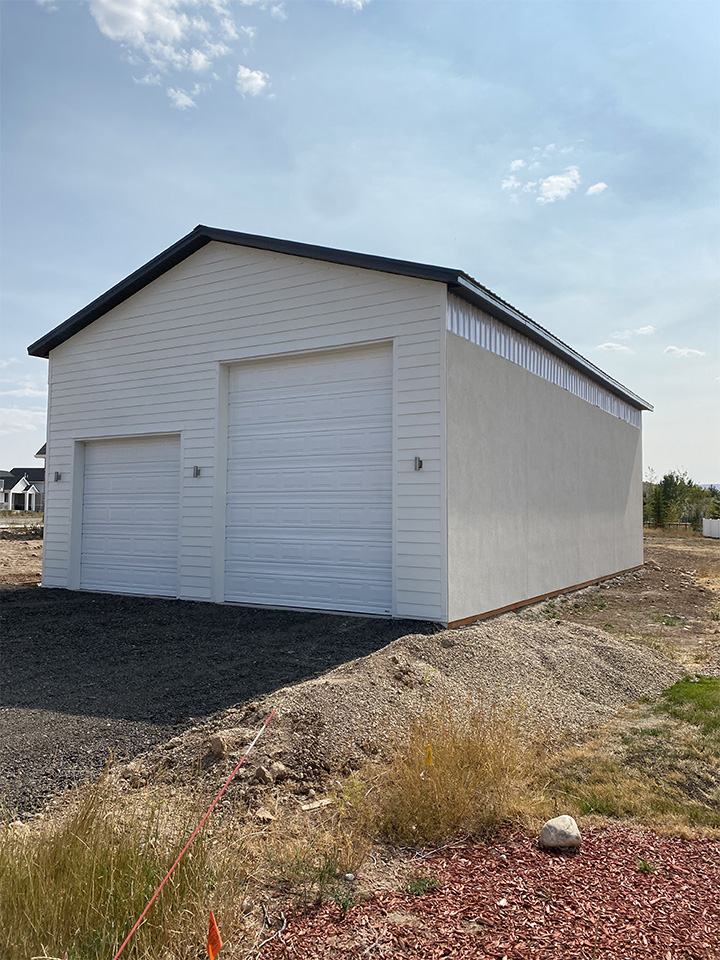 Image of a white pole barn with large garage doors, sitting on a gravel lot. Ideal for storage.