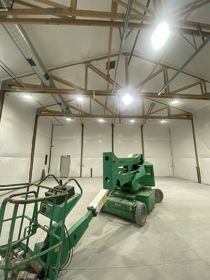 Inside view of a pole barn under construction, showing exposed beams and machinery.