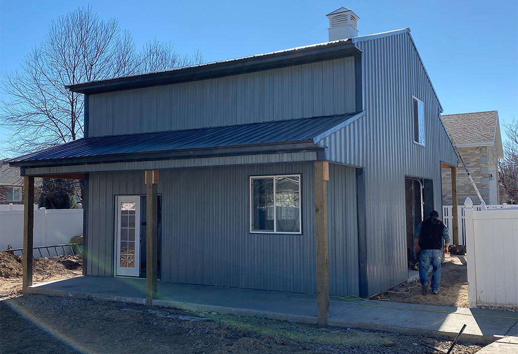 Image of a modern metal pole barn with a lean-to, windows, and a porch area under construction.