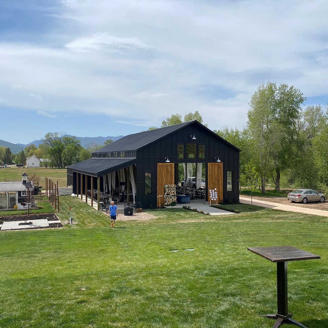 Image of a black pole barn with large open doors, windows, and an outdoor seating area.