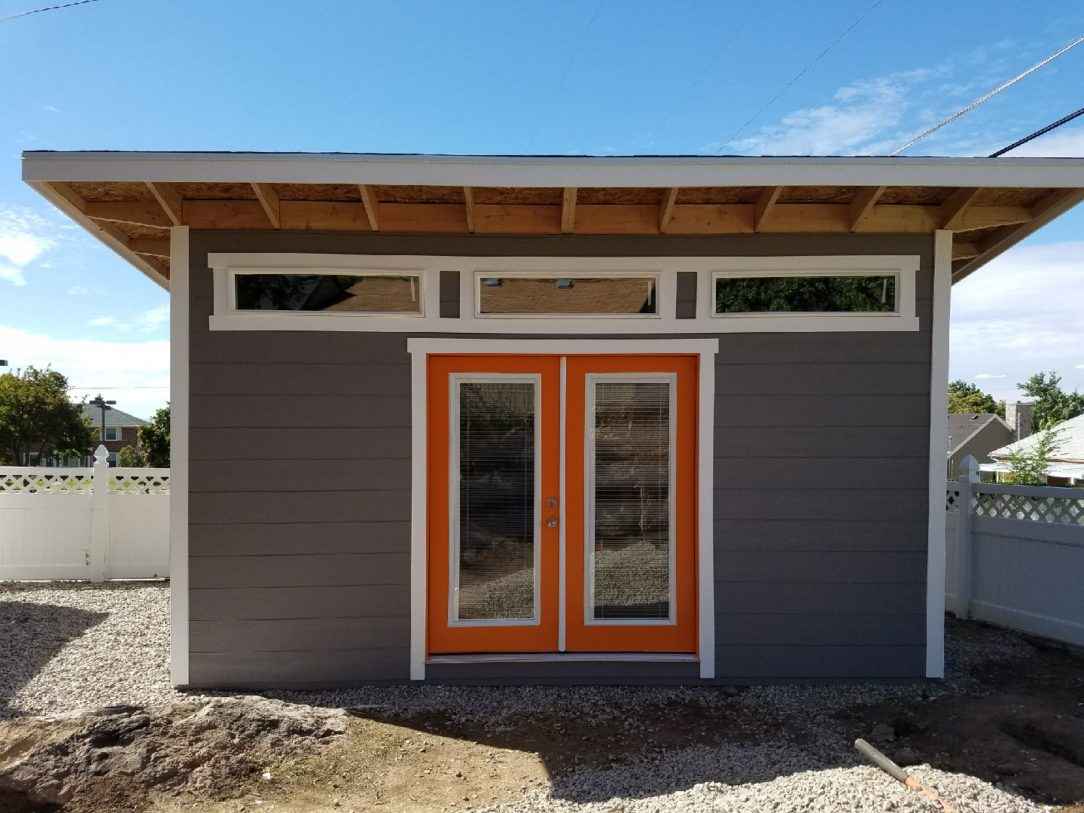 A sleek lean-to shed with orange double doors, large windows, and exposed overhangs.