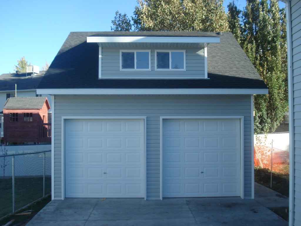 A spacious dormer garage with two white garage doors and a charming upper window.
