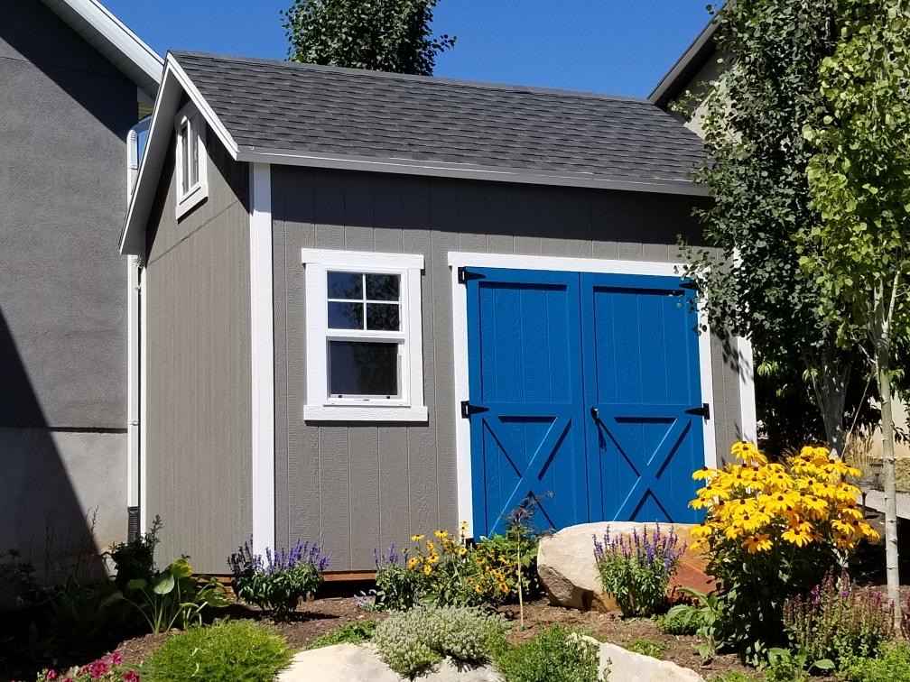 A custom orchard shed with blue double doors, white trim, and a landscaped garden.