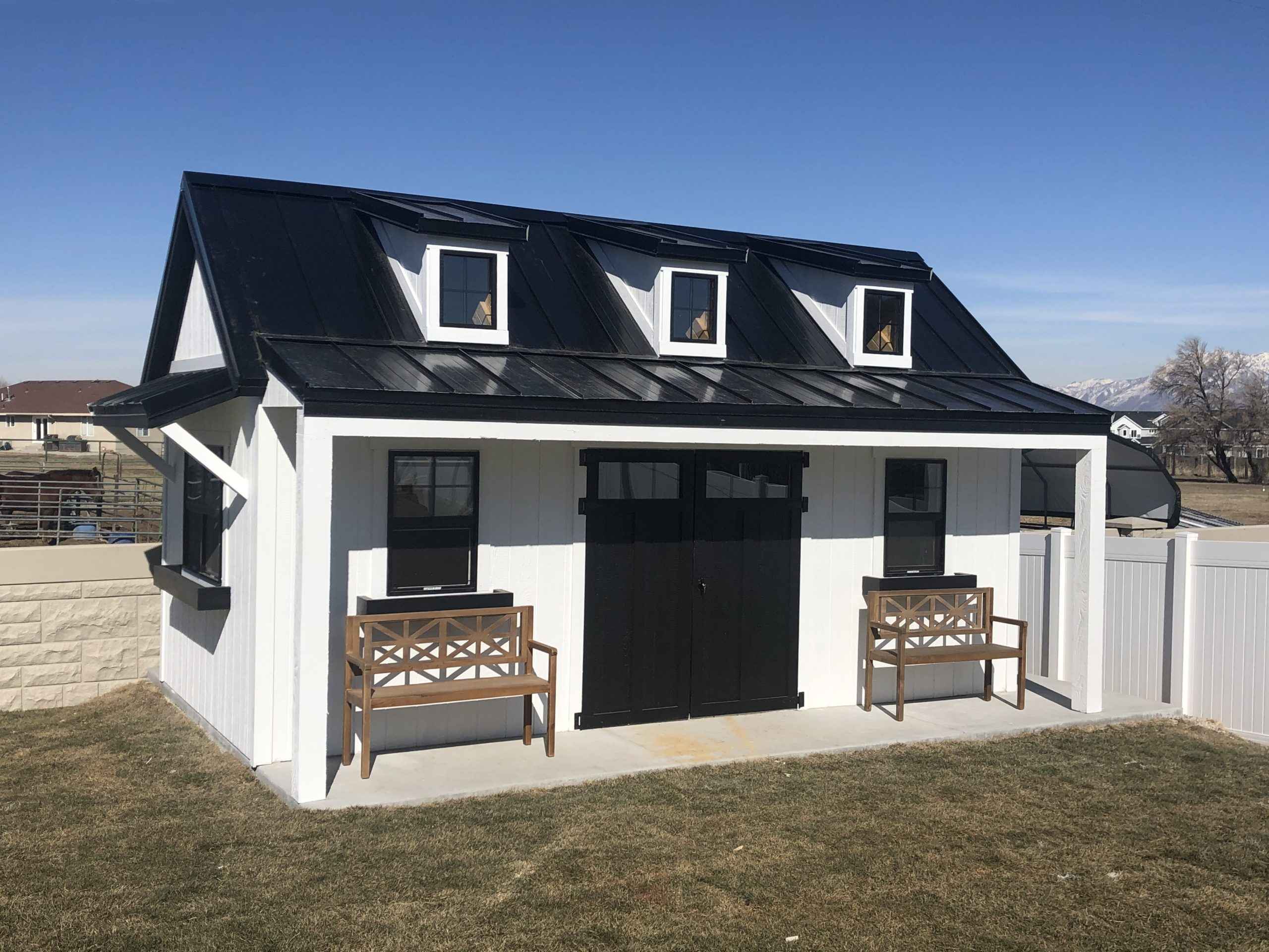 A modern black and white orchard shed with a flat roof dormer, featuring benches outside.